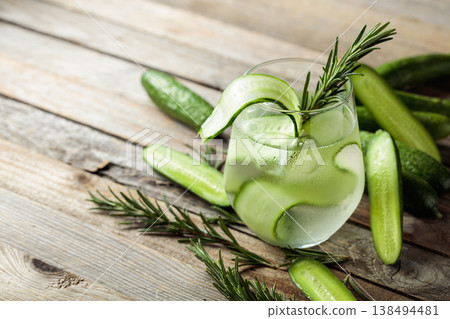 Gin tonic with ice, rosemary, and cucumber on an old wooden table. 138494481
