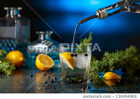 Gin is poured from a bottle into a glass with ice and lemon slice. Gin is poured from a bottle into a glass with ice and lemon slice. 138494908