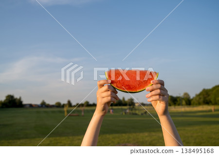 Juicy red watermelon slice in hand, on sunset park background Juicy red watermelon slice in hand, on sunset park background 138495168