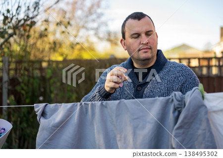 Man hangs up laundry to dry outdoors on hanging rope. Father performs home duties. Man hangs up laundry to dry outdoors on hanging rope. Father performs home duties. 138495302