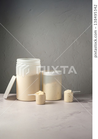 Protein powder in scoops with white plastic protein tubes, jars in background. Body building, muscle growth and food supplement concept Protein powder in scoops with white plastic protein tubes, jars in background. Body building, muscle growth and food supplement concept 138495342