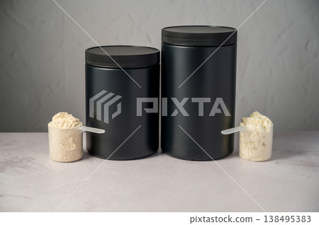 Protein powder in scoop with black protein tubes, jars in background. Body building, muscle growth and food supplement concept Protein powder in scoop with black protein tubes, jars in background. Body building, muscle growth and food supplement concept 138495383