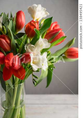 Spring floral background. Red tulips and Fresia white flower bouquet in glass vase. Copy space 138495421