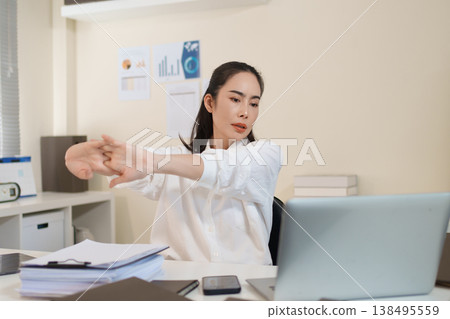 Businesswoman stretching arms to relieve work stress during busy office workday Businesswoman stretching arms to relieve work stress during busy office workday 138495559
