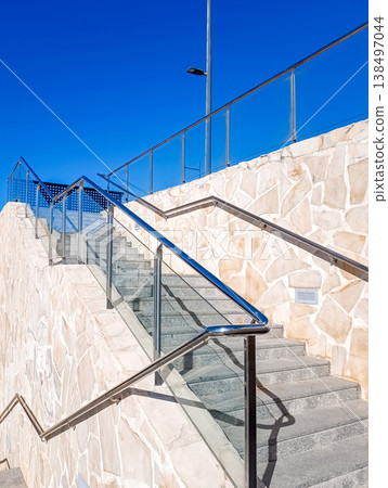 Stone Staircase with Glass Railings Viewed from Below Against Blue Sky Stone Staircase with Glass Railings Viewed from Below Against Blue Sky 138497044