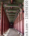 A long perspective view of iconic red wooden pillars decorated with traditional Korean Dancheong patterns in a royal palace hallway, featuring a person walking in the distance. 138498100