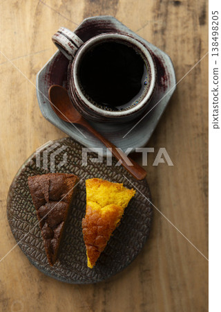 A black coffee in a ceramic mug and two kinds of cake (chocolate and pumpkin), a wooden spoon, and a view of a vintage wooden table. 138498205