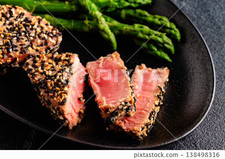 Tuna steak fried in sesame seeds served with asparagus. 138498316