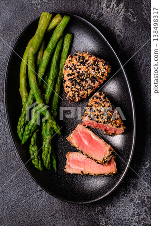 Tuna steak fried in sesame seeds served with asparagus. 138498317