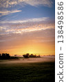 A peaceful summer morning landscape featuring a glowing sunrise over a mist-covered rural field.  138498586