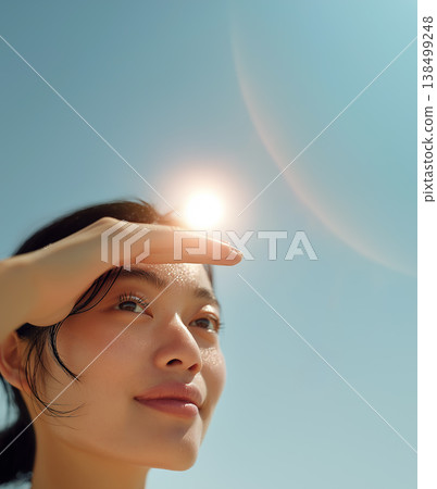 A young woman's profile as she shields herself from the sun, symbolizing summer UV protection and beautiful skin. 138499248