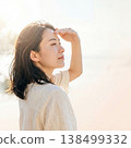 A woman shielding her eyes from the sun with her hands, an image representing protection against strong sunlight and summer UV rays. 138499332