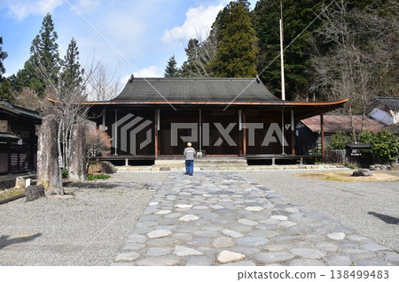 Shorenji Temple, a nationally designated important cultural property, in Takayama City, Gifu Prefecture, Japan: Beautiful Japanese architecture of the main hall and stone-paved approach; the back of a man praying. 138499483