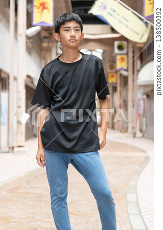 A teenage boy standing there in casual attire: a black T-shirt and jeans. 138500392