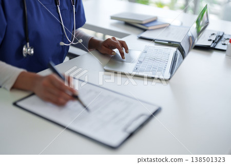 Adult medical professional working at hospital office desk managing patient data documents healthcare administration nurse doctor physician writing records Adult medical professional working at hospital office desk managing patient data documents healthcare administration nurse doctor physician writing records 138501323