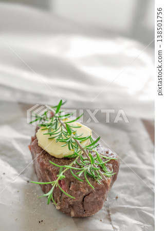 Single raw beef steak with rosemary and butter close up on parchment paper rustic kitchen Single raw beef steak with rosemary and butter close up on parchment paper rustic kitchen 138501756