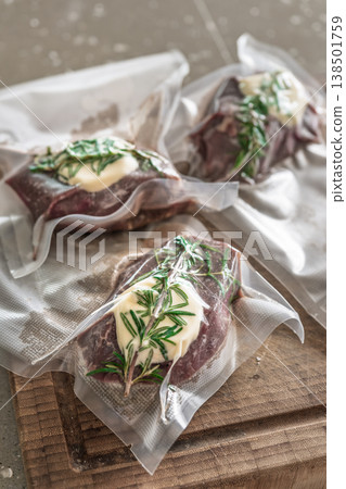 Three raw beef steaks with rosemary and butter in vacuum bags on wooden board sous vide Three raw beef steaks with rosemary and butter in vacuum bags on wooden board sous vide 138501759