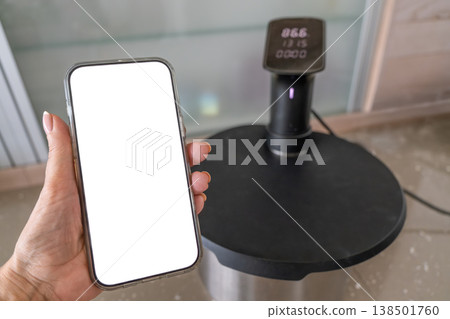 Smartphone controlling sous vide circulator on kitchen counter modern cooking technology Smartphone controlling sous vide circulator on kitchen counter modern cooking technology 138501760
