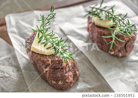 Two raw beef steaks with rosemary and butter on parchment paper over wooden board rustic kitchen Two raw beef steaks with rosemary and butter on parchment paper over wooden board rustic kitchen 138501951
