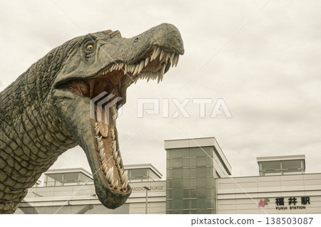 A photo of a dinosaur monument with its mouth wide open in the plaza at the west exit of JR Fukui Station. 138503087