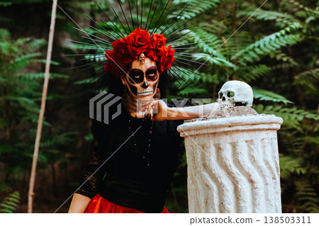 Day of the Dead. A woman with a wreath of red roses and a skull on a column. Artistic composition Day of the Dead. A woman with a wreath of red roses and a skull on a column. Artistic composition 138503311