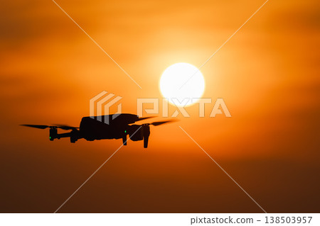 Drone silhouette flying in front of bright sun at sunset Drone silhouette flying in front of bright sun at sunset 138503957