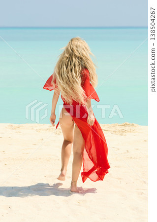 A beautiful tanned girl is wearing in red cape fun on the personal beach of the villa on a sunny day in the Maldives, she is happy and posing A beautiful tanned girl is wearing in red cape fun on the personal beach of the villa on a sunny day in the Maldives, she is happy and posing 138504267