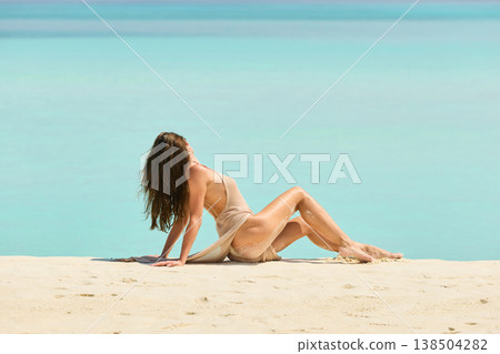 A beautiful tanned girl with an athletic physique in a swimsuit is siting on the beach on a sunny day in the Maldives, she is happy and posing A beautiful tanned girl with an athletic physique in a swimsuit is siting on the beach on a sunny day in the Maldives, she is happy and posing 138504282