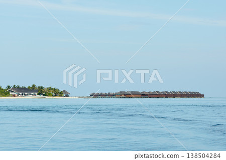 Classic Maldives island landscape on a sunny day, coastal luxury resort buildings, azure water, white sand, palm trees on the shore 138504284
