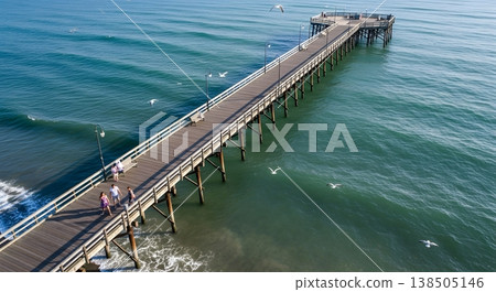Aerial View Of Wooden Pier Extending Into Turquoise Ocean With People And Birds On A Sunny Day 138505146