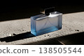 Perfume Bottle with Black Cap on Concrete Surface Under Sunlight with Dramatic Shadow and Blue Liquid 138505544