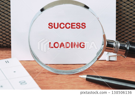 Red SUCCESS LOADING on a document, set on a wooden desk with office essentials, signaling hopeful progress 138506136