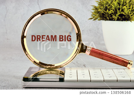 Golden magnifier on white calculator keyboard enlarges Dream Big. Bright desk, lush green plant nearby Golden magnifier on white calculator keyboard enlarges Dream Big. Bright desk, lush green plant nearby 138506168