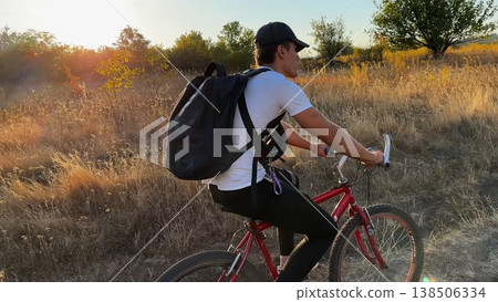 Happy young man ride mountain ski bike along trail on sunny summer day. Beautiful golden sunlight at background. Concept of active lifestyle, adventure spirit and carefree weekend outdoor Happy young man ride mountain ski bike along trail on sunny summer day. Beautiful golden sunlight at background. Concept of active lifestyle, adventure spirit and carefree weekend outdoor 138506334