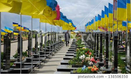 Mourning man go among countless graves of ukrainian soldiers with national flags at military cemetery in Kharkiv. Scene reflects personal sorrow and nation collective loss caused by russian aggression Mourning man go among countless graves of ukrainian soldiers with national flags at military cemetery in Kharkiv. Scene reflects personal sorrow and nation collective loss caused by russian aggression 138506350