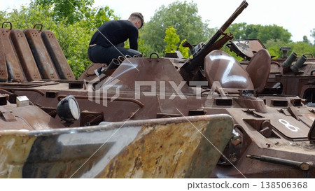 Young man looking at destroyed military equipment of the russian army. Exhibition of rusty and burned-out armored vehicles on ukrainian territory. War between Ukraine and russia. Slow motion Young man looking at destroyed military equipment of the russian army. Exhibition of rusty and burned-out armored vehicles on ukrainian territory. War between Ukraine and russia. Slow motion 138506368