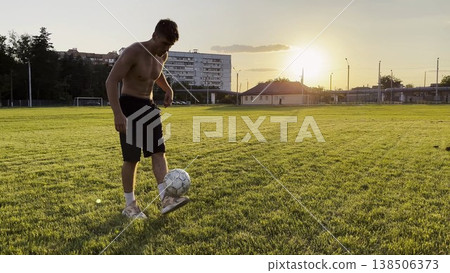 Young man juggling soccer ball on stadium at sunset. Professional footballer kicking ball at green field. Sportsman practicing tricks at meadow with sunlight at background. Freestyle football 138506373