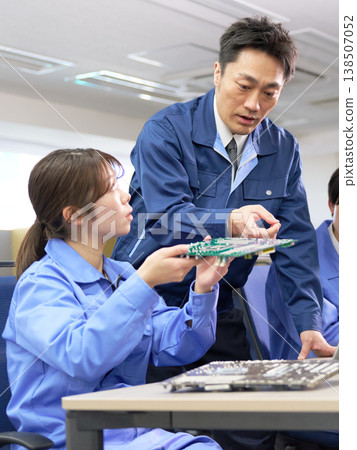 Technical training for young employees learning by looking at circuit boards, with their supervisors providing guidance. 138507052