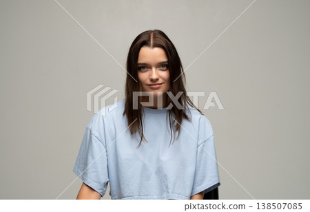 Young lady with brunette hair posing in a sky blue crop top, smiling warmly at the camera against a simple backdrop Young lady with brunette hair posing in a sky blue crop top, smiling warmly at the camera against a simple backdrop 138507085