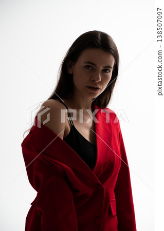 Woman model posing in studio, wearing a red blazer draped over shoulders, showcasing fashion, style, beauty, and confidence with a moody low key lighting effect 138507097