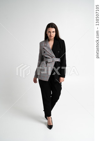Woman standing confidently, showcasing a unique half plaid, half black blazer with a belt, embodying a stylish and conceptual blend of patterns and colors Woman standing confidently, showcasing a unique half plaid, half black blazer with a belt, embodying a stylish and conceptual blend of patterns and colors 138507105