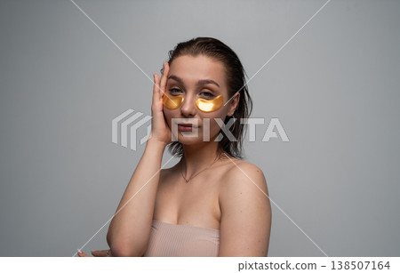 Young woman applying golden eye patches for a delicate under-eye skin treatment, embracing cosmetic care, hydration, and self-care routine at home 138507164