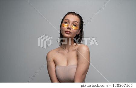 Young woman applying luxurious gold eye patches for under eye skin care, embracing beauty rituals, self-care, and wellness at home, looking at camera Young woman applying luxurious gold eye patches for under eye skin care, embracing beauty rituals, self-care, and wellness at home, looking at camera 138507165