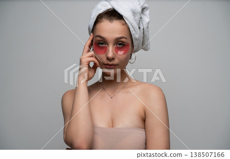 Young woman completing beauty routine, applying under eye patches, wearing a towel on her hair for refreshing skincare, feeling calm and practicing self-care at home Young woman completing beauty routine, applying under eye patches, wearing a towel on her hair for refreshing skincare, feeling calm and practicing self-care at home 138507166