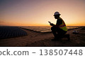 Field technician carefully examines solar panel connectors against warm evening sky 138507448