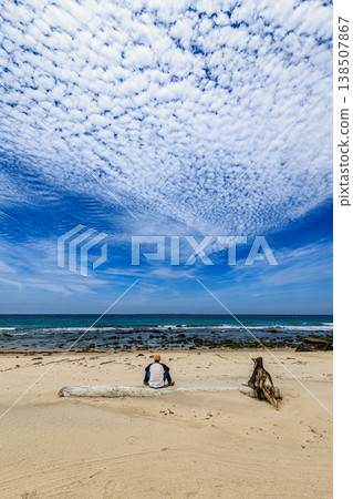 蔚藍的大海，佈滿卷積雲的天空，以及坐在沙灘上的人的背影。 138507867