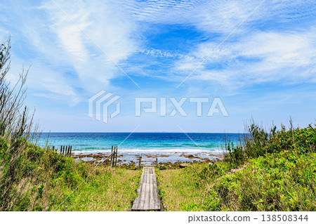 A wooden boardwalk through a grassland, a path leading to the sea, and a beautiful sky filled with cirrocumulus clouds. A wooden boardwalk through a grassland, a path leading to the sea, and a beautiful sky filled with cirrocumulus clouds. 138508344