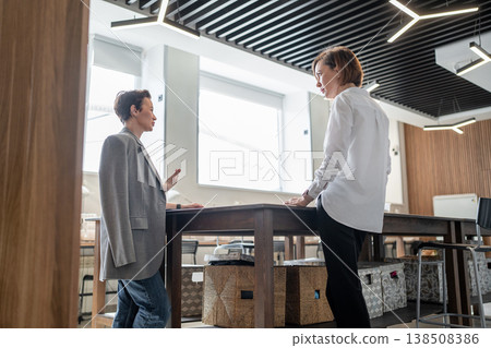 Businesswomen standing and planning together at tall table in spacious modern light office. Planning, standing, table, modern, office, teamwork, businesswomen. Businesswomen standing and planning together at tall table in spacious modern light office. Planning, standing, table, modern, office, teamwork, businesswomen. 138508386