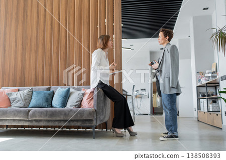 Women interacting and having informal discussion on sofa in stylish open office workspace. Interaction, discussion, teamwork, sofa, office, businesswomen. Women interacting and having informal discussion on sofa in stylish open office workspace. Interaction, discussion, teamwork, sofa, office, businesswomen. 138508393