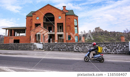 Motorcyclist passes by unfinished red brick house on sunny day Motorcyclist passes by unfinished red brick house on sunny day 138508407
